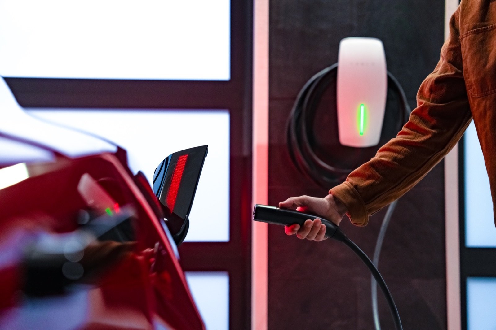 A hand plugging the Tesla Wall Connector cable into a Tesla Model 3's charge port