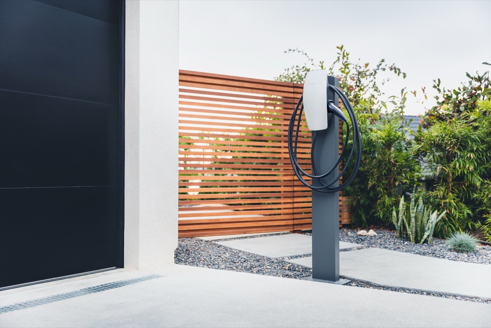 Tesla Wall Connector mounted on an outdoor pedestal beside a house's driveway